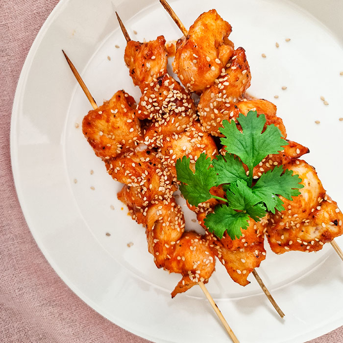 Airfryerissa kypsennetyt valkosipuli-gochujang kanavartaat lautasella. Vartaiden paalla on vaaleita seesaminsiemenia ja tuoretta korianteria.